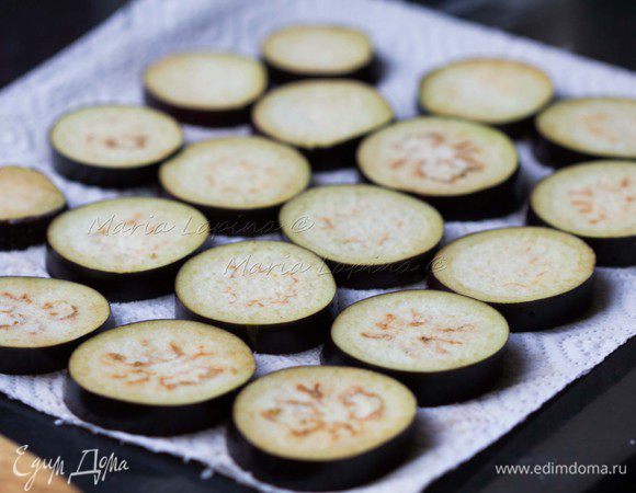 Баклажаны вымыть и нарезать ломтиками примерно по 0,5 см. Разложить их на бумажном полотенце и посолить. Сверху накрыть еще одним слоем бумажных полотенец и поставить сверху что-нибудь потяжелее в качестве груза, например, противень или доску. Оставляем на 30–40 минут. Это нужно для того, чтобы баклажаны отдали лишний сок, тогда они впитают меньше масла при обжарке и не будут горчить.