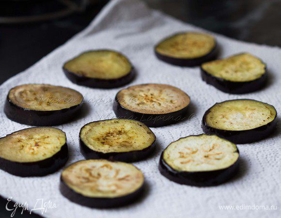 Баклажаны промокнуть насухо, обжарить с обеих сторон до золотистого цвета на оливковом масле. Обжаренные баклажаны выкладывать на бумажное полотенце, чтобы оно впитало излишки масла.