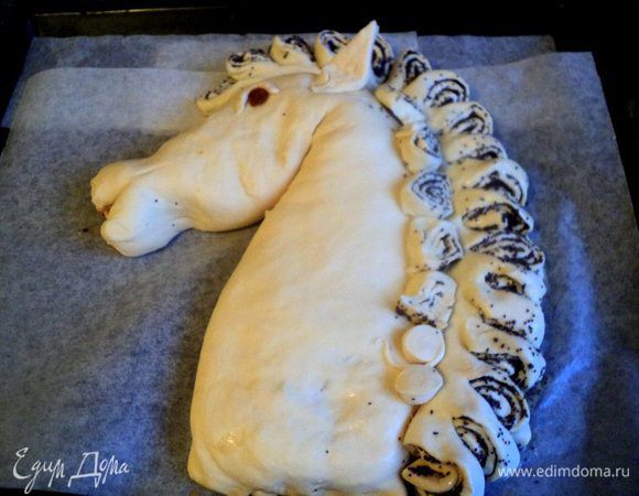 Затем маковые рулетики повернуть, чтобы была видна начинка, получим гриву лошади. Из кусочков теста сформировать ушки и глаз лошади, изюминка – зрачок. В таком виде поставить противень с пирогом в теплое место для расстойки и подъема теста. Я ставила в духовку, нагретую до 50 градусов.
