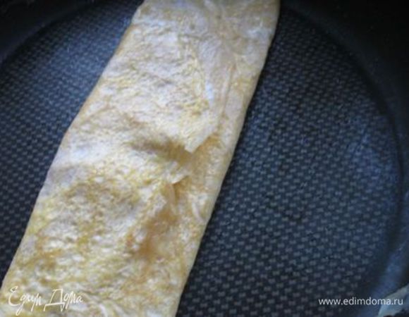  С помощью деревянных палочек или лопатки свернуть омлет в рулет ( ширина -5-6 см)  и сдвинуть его на  край сковороды.