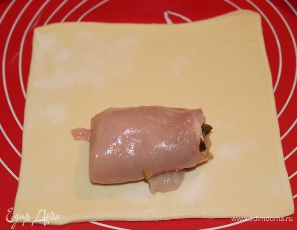 Слоеное тесто разморозить согласно инструкции на упаковке. На посыпанном мукой столе слегка раскатать тесто и разрезать его на 4 квадрата. В центр каждого квадрата выложить куриный рулетик. 