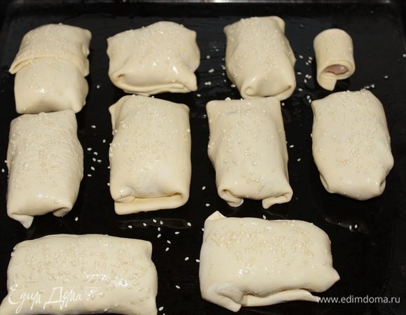 Загнуть углы теста в виде конвертика, смазав края теста водой. Приготовленные конвертики выложить на  противень швом вниз. Смазать взбитым яйцом, посыпать кунжутными семечками.