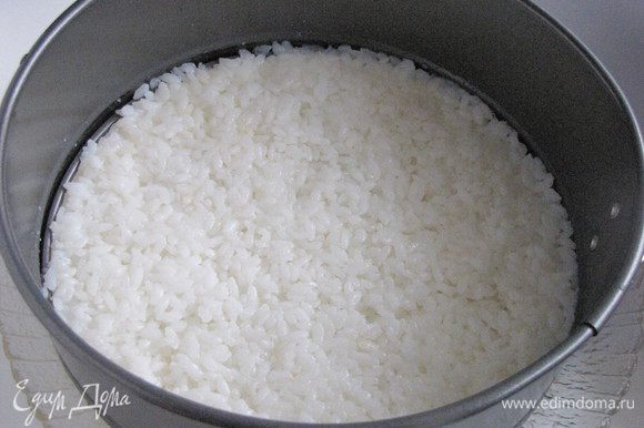 Взять кольцо от разъемной формы для торта диаметром 18-20 см и поставить на блюдо. Выложить половину риса равномерно, тонким слоем, смачивая руки водой.