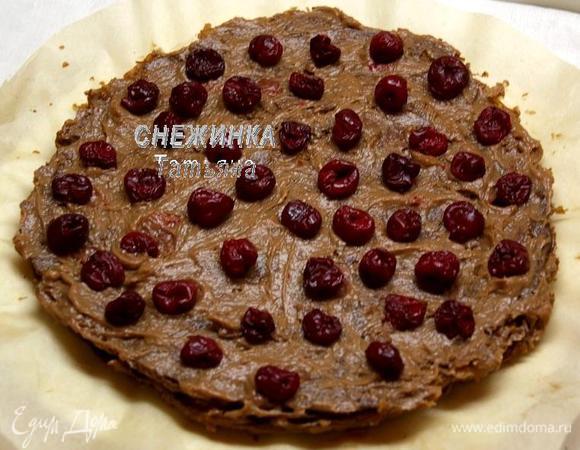 Собираем торт. Удобнее это делать на тарелке, которая выстелена пергаментом, потому что в процессе сборки можно вымазать всё вокруг, а так затем бумага хорошо извлекается и мы переместим торт на красивое блюдо. Берём один корж, стараемся выбрать один из самых ровных. Промазываем небольшим количеством крема, слегка надавливая на него ложкой, чтобы он осел. Кладём второй корж, прижимаем слегка руками, чтобы он достаточно плотно лёг на первый. Не боимся, когда тесто хрустит! Поскольку края в любом случае не будут точь-в-точь как у первого коржа, слегка отщипываем тесто по краю, чтобы сравнять его с первым. Крошку сохраняем. Промазываем кремом и на этот второй корж кладём вполовину вишни. 