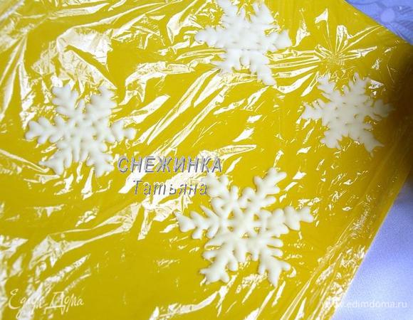 Для украшения растапливаем на водяной бане белый шоколад. Затем даём ему остыть, чтобы он не был слишком жидким, а был как бы тягучим. Перекладываем растопленный шоколад в кондитерский шприц или в пакетик (файл), у которого затем отрезаем уголок, сделав маленькую дырочку. На доску стелим пищевую плёнку, зафиксировав края. Рисуем на плёнке шоколадом снежинки, можно воспользоваться трафаретом снежинки, заранее распечатанным или нарисованным, и подложив трафарет под пищевую плёнку. Отправляем заготовки застыть в холодильник.