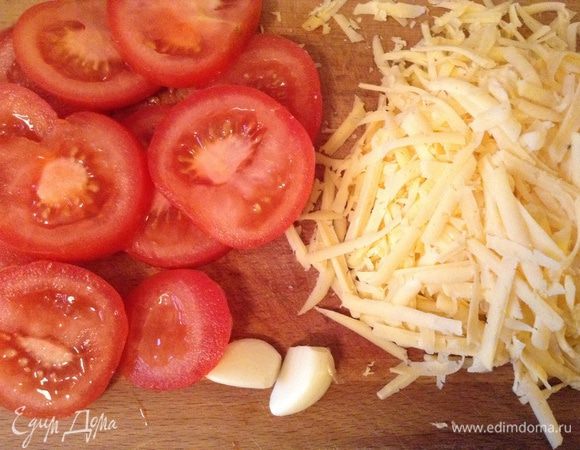 Тем временем порезать помидоры продольно, потереть сыр и очистить чеснок.