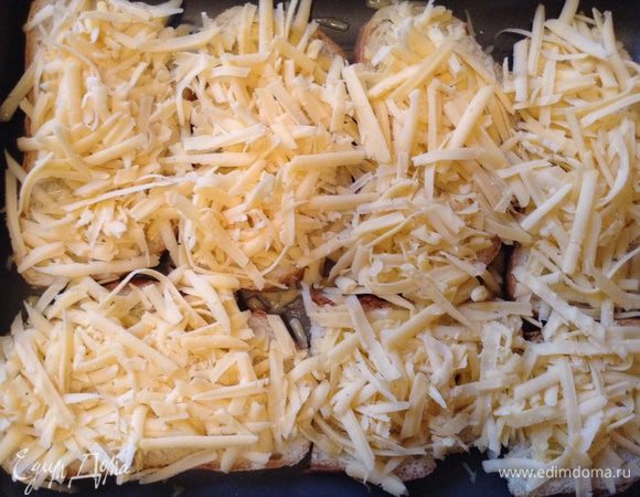 Вынуть из духовки протвень и уложить на бутерброды первым слоем сыр, затем раздавленный чеснок.