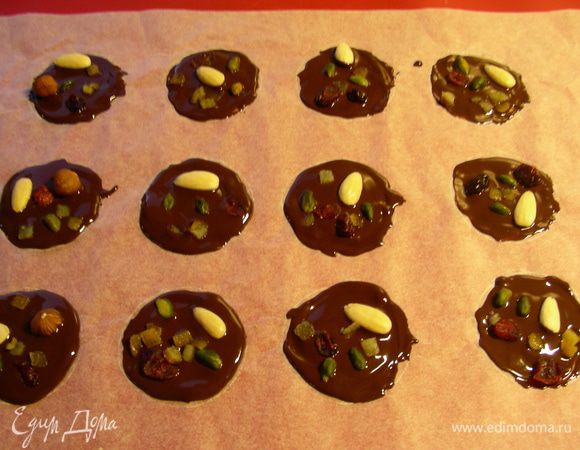 Небольшой противень выстилаем бумагой для выпечки. Рисуем (у кого глаз наметан может этого не делать) 12 небольших кругов или овалов (я использовала стакан). Ложкой выкладываем шоколад по намеченным формам. Пока шоколад еще жидкий, выкладываем на него по 1 штучке  вида сухофруктов, слегка их вдавливая. Можно и побольше положить, как сделала я. Оставляем остывать, а затем отправляем в холодильник на 20 минут.
