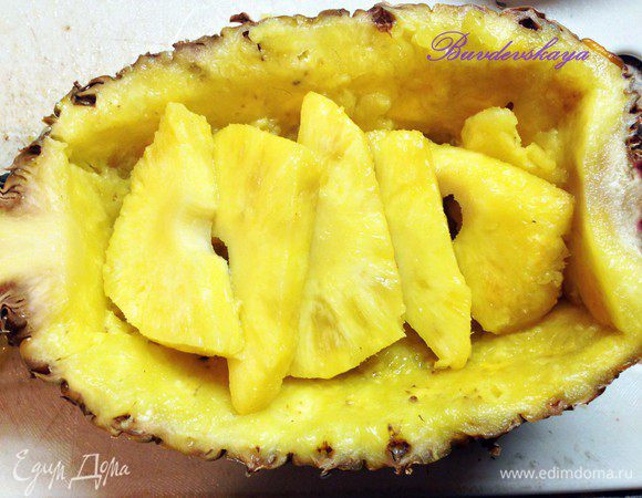 Тем временем подготавливаем наш ананас. Моем его и разрезаем вдоль на 2 половины. Аккуратно вырезаем мякоть, превращая ананас в сервировочное блюдо. Из мякоти вырезаем жесткую сердцевину и нарезаем ананас дольками. Выкладываем дольки в обратно в ананас.