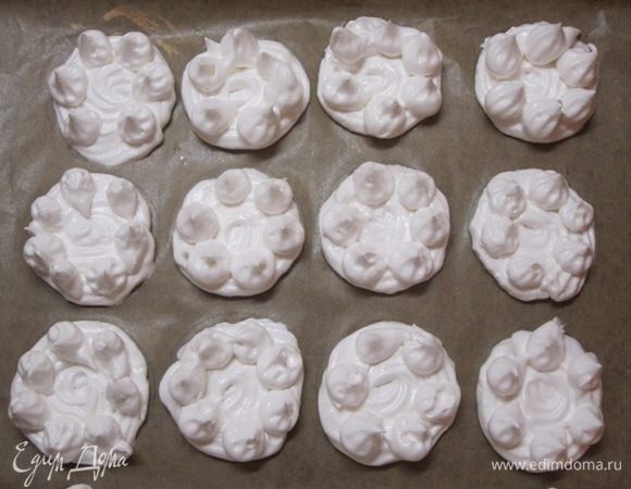 Взбитыми белками наполнить кондитерский шприц. Отсадить на противень, выстланный бумагой для выпечки, 20 донышек спиралевидной формы диаметром 6 см.  На каждое донышко отсадить капельки взбитых белков.