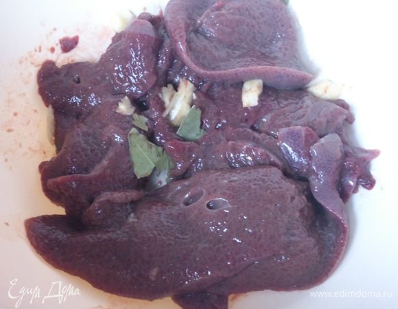 Сложить печень в миску, посыпать раздавленным чесноком и лавровым листом 