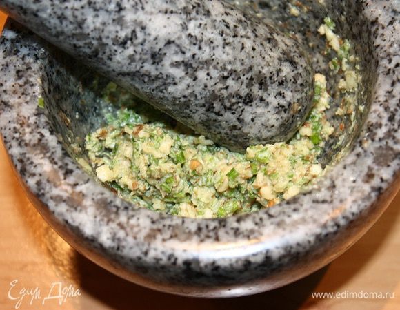 Теперь начинка. В ступке растереть грецкие орехи с солью. Орехи выделят свое масло. После этого добавить чеснок, половину зелени петрушки и перетереть.