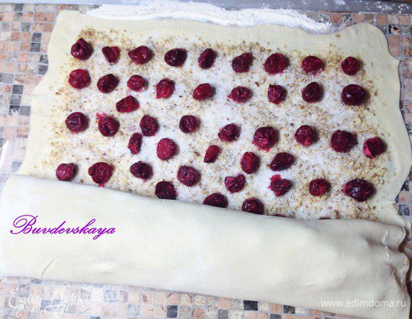 Поверх орехов выложить вишню и посыпать сахарным песком. Аккуратно свернуть рулетом как можно плотнее. Выложить на противень, застеленный силиконовым ковриком или пергаментом. Сделать несколько наколов вилкой и смазать взбитым яйцом. Поставить в разогретую до 200°C духовку минут на 15, до образования золотистой корочки. Вынуть из духовки, немного остудить, посыпать сахарной пудрой. Подавать к чаю или кофе с шариком ванильного мороженого.