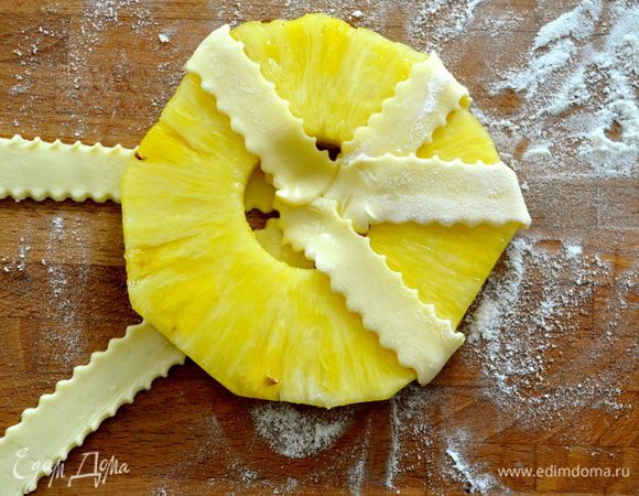 Кружочки ананса выложить на тесто и обмотать полосками, завернув концы к центру. Прижать в центре пальцем.
