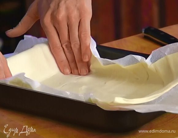 Небольшую форму для выпечки выстелить пищевой бумагой и уложить в нее пласт теста так, чтобы края немного свешивались.