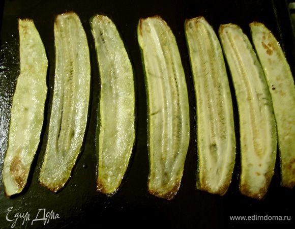 Чеснок выдавить через пресс. На противне разогреть оливковое масло и припустить выдавленный чеснок 3 минуты. Цукини нарезать на ломтики 5 мм. Выложить ломтики цукини на противень и запекать в духовке с обеих сторон до подрумянивания.