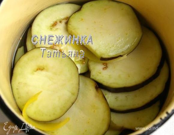 В кастрюле соединяем воду и 150 г сахара. Добавляем цедру лимона, я прямо ножом срезала кусочки цедры, без белой мякоти. Ставим на огонь и доводим до кипения, чтобы сахар растворился. Баклажан моем хорошо, нарезаем не очень тонкими и не толстыми кружочками. Кладём нарезанный баклажан в сироп.