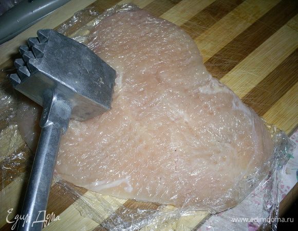 Теперь нам надо слегка отбить мясо. Удобно это сделать с помощью пищевой пленки. Застилаем разделочную доску пищевой пленкой, кладем подготовленное филе, накрываем пищевой пленкой и отбиваем его молотком.