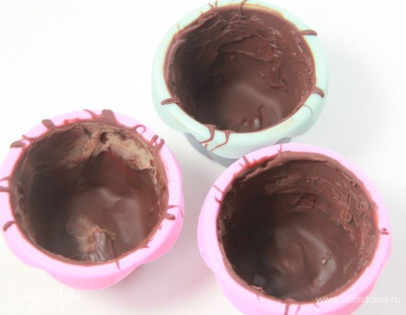 Силиконовые стаканчики смазать растопленным шоколадом (я растапливаю в микроволновке, на высокой мощности примерно минуту, периодически помешивая), убрать на 15 минут в морозилку. Проделать эту же процедуру ещё раз.
