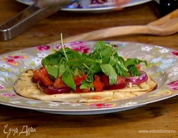 Обжаренную лепешку поместить на тарелку, посыпать натертым сыром, выложить кольца лука, затем кусочки помидора и заправку из руколы.