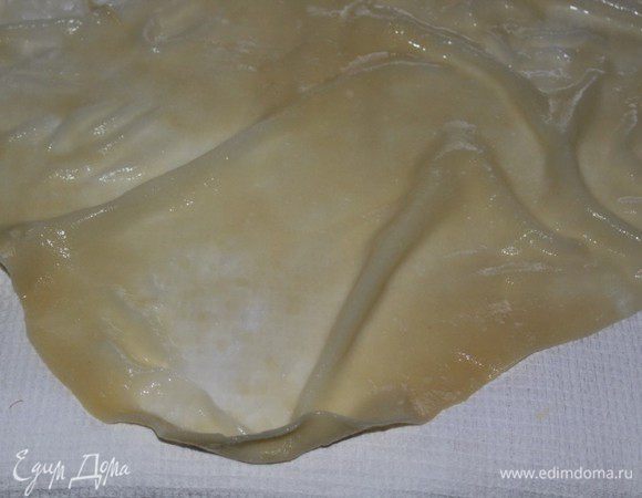 Тесто разделить на 5 частей - 4 одинаковые и одна немного больше остальных.  Раскатать бОльшую часть теста в тонкую лепешку. Приготовить две кастрюли - одну с кипятком, вторую с холодной водой. Опустить лепешку в кипящую подсоленную воду на 30-40 секунд, затем быстро опустить в холодную и откинуть на дуршлаг. Дать воде стечь, затем переложить на вафельное х/б полотенце и промокнуть от лишней воды.