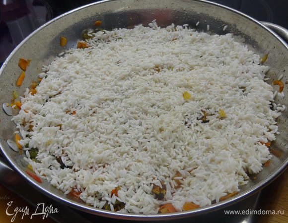 Рис предварительно замочить в холодной воде на 15 минут. Затем слить и добавить к овощам, рыбе и морепродуктам. Равномерно распределить по всему диаметру сковородки.  
