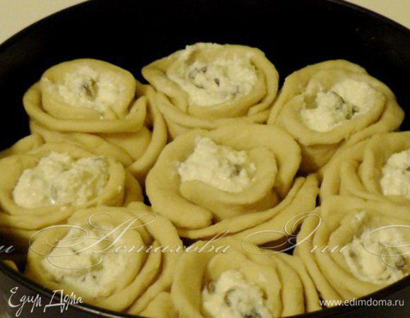 Затем получившиеся розочки выкладываю в форму для выпечки, предварительно смазанную маслом. Смазываю поверхность пирога взбитым желтком и присыпаю кунжутом.