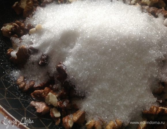 Через пару минут к орехам добавить сахар и жарить, непрерывно помешивая лопаткой.