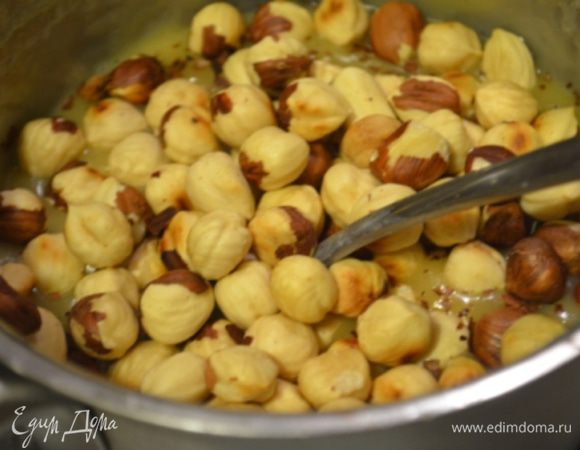 Пока варится нуга, фундук обжарить на сковороде и очистить от кожуры, в готовую нугу добавить орехи и перемешать.
