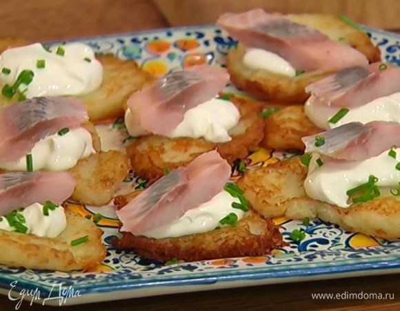 Горячие драники выложить на тарелку, намазать сметаной, посыпать шнитт-луком, сверху разложить кусочки сельди.