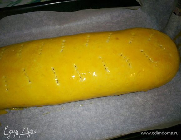 С помощью бумаги или пергамента сворачиваем наше тесто рулетом. Защипываем края. Рулет накалываем вилкой, чтоб он не лопнул во время выпекания. Оставшийся от приготовления теста яичный желток смешиваем с водой и смазываем рулет.