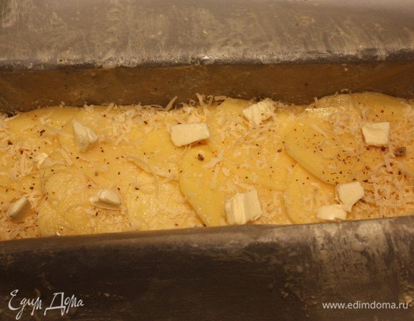 Форму выкладываем бумагой для выпекания, промазанной сливочным маслом. Затем выкладываем картофель внахлест. Каждый слой посыпаем приправой для картофеля и тертым сыром и кладем кусочки сливочного масла. Солить через слой. Когда доходим до среднего слоя, выдавливаем чеснок через чеснокодавку, затем сыр и масло. Когда все слои выложены, залить 100 мл сливок.