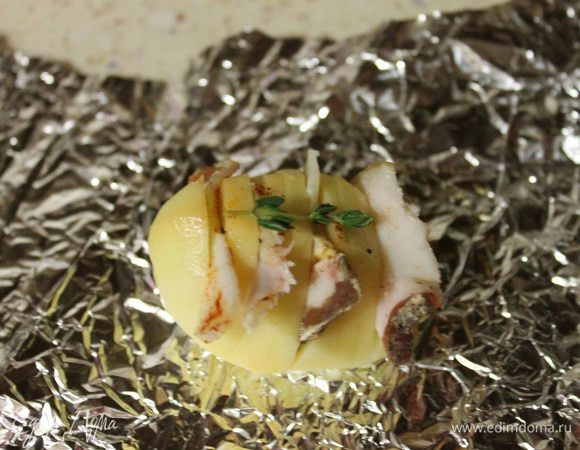 В разрезы картошки вставить по ломтику сала. Берем фольгу, на середину выкладываем по небольшому кусочку сливочного масла, сверху кладем картошечку, посыпаем травками и заворачиваем, как мешочек.