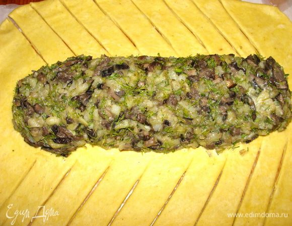 Кусочек теста оставить для декора. Основную часть раскатать в пласт прямоугольной формы толщиной 4-5 мм. В середину выложить начинку. Сделать надрезы ножом. Ширина полосок 2.5-3 см.