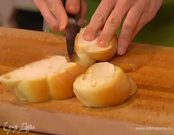 Булку нарезать на 5–6 толстых ломтиков и надрезать их сбоку вдоль, не прорезая до конца, так чтобы получились кармашки.