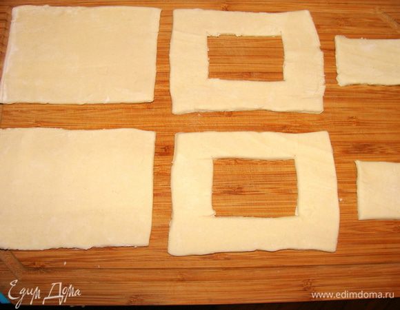 Тесто готовое разморозить. Разрезать на 16 одинаковых прямоугольников или квадратов, а можно и кружков. Можно приготовить пирожки еще более маленького размера (у меня были довольно крупные), тогда разделить еще на 2 и получится 32 квадратика на 16 порций. Пирожки закусочные, приближенные по значению к канапешкам. Половину квадратиков оставить, лишь немного раскатать, у второй половины вырезать внутри квадратики меньшего размера.