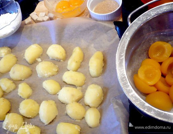 Картофель отварить в мундире в подсоленной воде. Лимонную цедру натереть. Духовку разогреть до 150 градусов. Подготовить желтки, сахар и крахмал. Абрикосы выложить на сито и дать жидкости стечь, затем промокнуть их бумажным полотенцем. Картофелю дать пару минут остыть и еще горячим очистить и разрезать вдоль на половинки. Выложить на противень, застеленный пекарской бумагой, и отправить в духовку «выпустить пар» на 8 минут. 