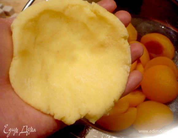 Каждый колобок положить на одну ладонь и прижать второй ладонью, чтобы образовалась  лепешка. На каждую лепешку выложить по абрикосу, сложенному из двух половинок и начиненному кусочком сахара. 