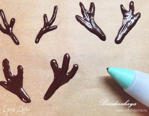 5. Делаем рога и глаза оленю. Растапливаем на водяной бане или в микроволновке темный шоколад и при помощи зубочистки рисуем на бумаге для выпечки рога. Внимание! Рога должны быть толщиной 3-4 мм, чтобы они не растаяли от прикосновения рук. На миндальных лепестках рисуем шоколадом кружочки. Отправляем рога и глаза в морозилку минут на 5-7.