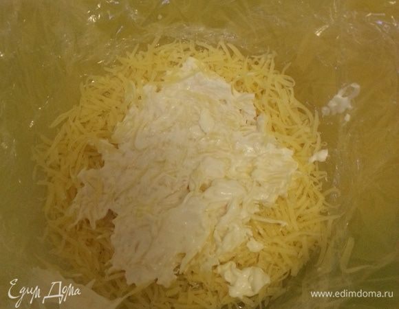 Выстилаем чашу пищевой пленкой, так чтобы края свисали. Выкладываем первый слой - твердый сыр, тертый на средней терке. Выкладываем столовую ложку чесночного майонеза.