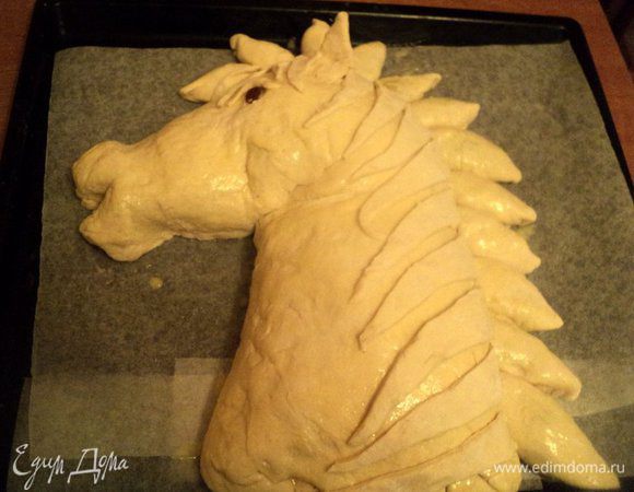 Из пирожков выложить пряди гривы. Из кусочков теста сформировать ушки и глаз лошади, изюминка – зрачок. В таком виде поставить противень с пирогом в теплое место для расстойки и подъема теста. Я ставила в духовку, нагретую до 50 градусов.