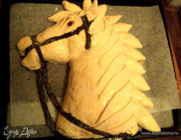 Пельменное тесто раскатать в пласт толщиной 2 мм, посыпать маком, прикатать скалкой и вырезать детали сбруи и уздечки. После расстойки пирога еще раз поправить тесто, формируя голову лошади. Смазать пирог взбитым яйцом. Наложить полоски из пельменного теста в виде уздечки. Выпекать в духовке при температуре 180 градусов 45 минут. Если верх начнет слишком румяниться, накрыть фольгой.