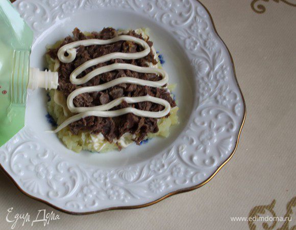 Говядину нарежем мелко и выкладываем сверху. И снова сеточкa, не забываем слегка посолить слои.Далее у нас идет нарезанный лук. Его надо заранее обдать кипятком. Сверху также сетка из майонезa.