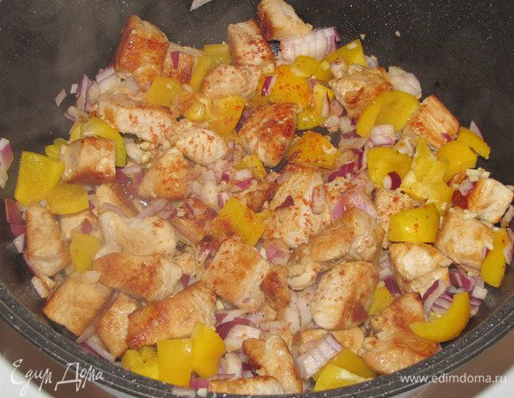 Затем вернуть все мясо в кастрюлю, добавить лук, чеснок и сладкий перец, а так же немного острого красного перца. Перемешать, закрыть крышкой и готовить на среднем огне 15 минут, время от времени помешивая.