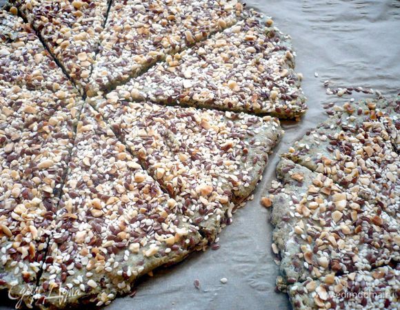 Духовку разогреваем на 160 градусов. Тесто делим на три шарика. Каждый раскатываем в тонкую лепешку шириной примерно 5 мм, у меня получилось немножко толще, поэтому пришлось увеличить время выпечки минут на 5, лучше все-таки потоньше, так хлебцы более хрустящие получаются. Выложим лепешки на застеленный пергаментом противень. Для посыпки лесной орех порубим мелко и обжарим на сухой сковороде. Смешаем с льняным семенем и кунжутом. По лепешкам проведем хорошо смоченной в воде кисточкой и посыпем обсыпкой, немного прижмем ее к лепешкам. Разрежем каждую лепешку на сегменты. Ставим в духовку на 35 минут (время указываю для тонких лепешек). Я еще оставляла хлебцы для большей хрусткости в духовке под пергаментом, пока духовка не остыла.