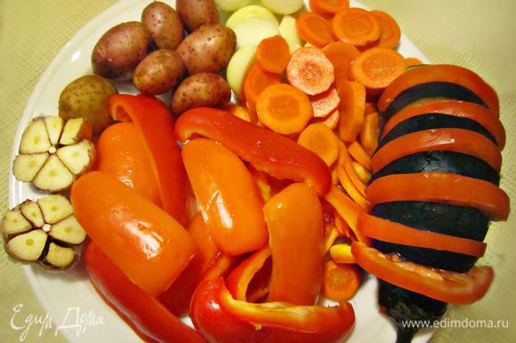 Подготовить овощи для запекания. Нарезать кружочками морковь, помыть картофель. У меня были картофелинки-мини, и я оставила их для запекания в кожуре. Крупных же картофелин потребуется, конечно, меньше и лучше их почистить и разрезать пополам. Далее необходимо будет нарезать крупными дольками перец, баклажан начинить круглыми дольками помидора, лук нарезать дольками, головку чеснока разрезать пополам. Посолить и сбрызнуть овощи маслом.