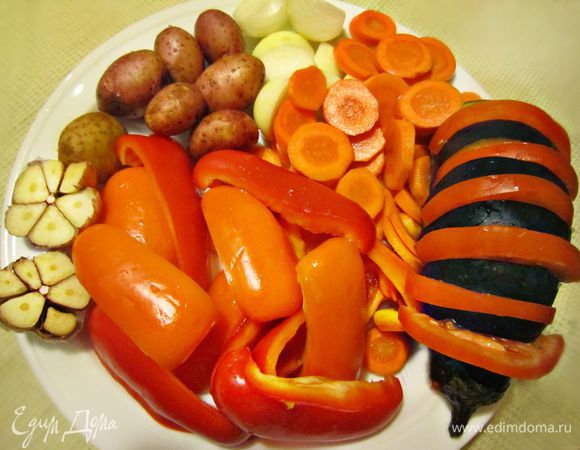 Подготовить овощи для запекания. Нарезать кружочками морковь, помыть картофель. У меня были картофелинки-мини, и я оставила их для запекания в кожуре.  Крупных же картофелин потребуется, конечно, меньше и лучше их почистить и разрезать пополам. Далее необходимо будет нарезать крупными дольками перец, баклажан начинить круглыми дольками помидора, лук нарезать дольками, головку чеснока разрезать пополам. Посолить и сбрызнуть овощи маслом.