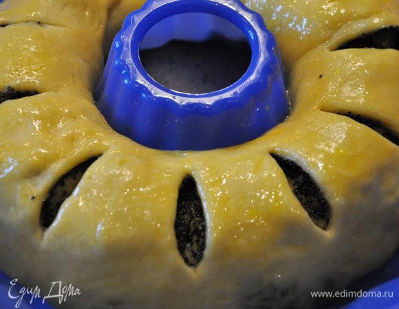Тесто раскатать в форме круга. Распределить начинку по всей поверхности. Плотно свернуть рулетом и положить в форму для кекса, скрепив концы. Смазать желтком с сахаром. Сделать ножом надсечки.