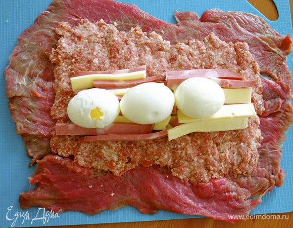 На подготовленную мясную мякоть выложить ровным слоем фарш. Разровнять, оставляя по краям примерно 2 см без начинки, чтобы при скручивании рулета начинка не вышла из него. Сверху и посередине выложить все остальные компоненты начинки; мортаделлу, сыр и сало (если Вы его используете!) В самом конце сверху положить в ряд вареные яйца!