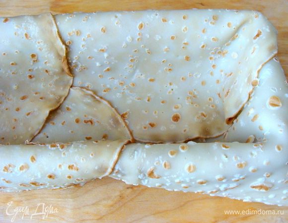 Форму для выпечки хлеба выложить блинами так, чтобы края сильно свешивались. Смазать теплым сливочным маслом.